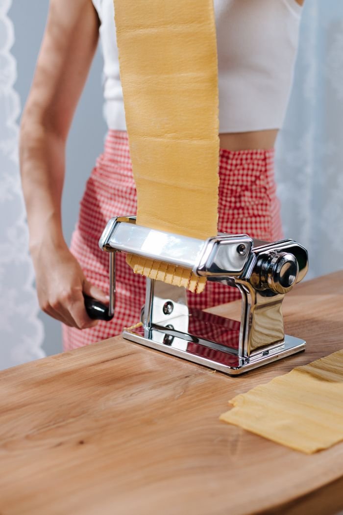 category-01 Woman using a pasta maker to create fresh sheets of pasta in a kitchen setting.